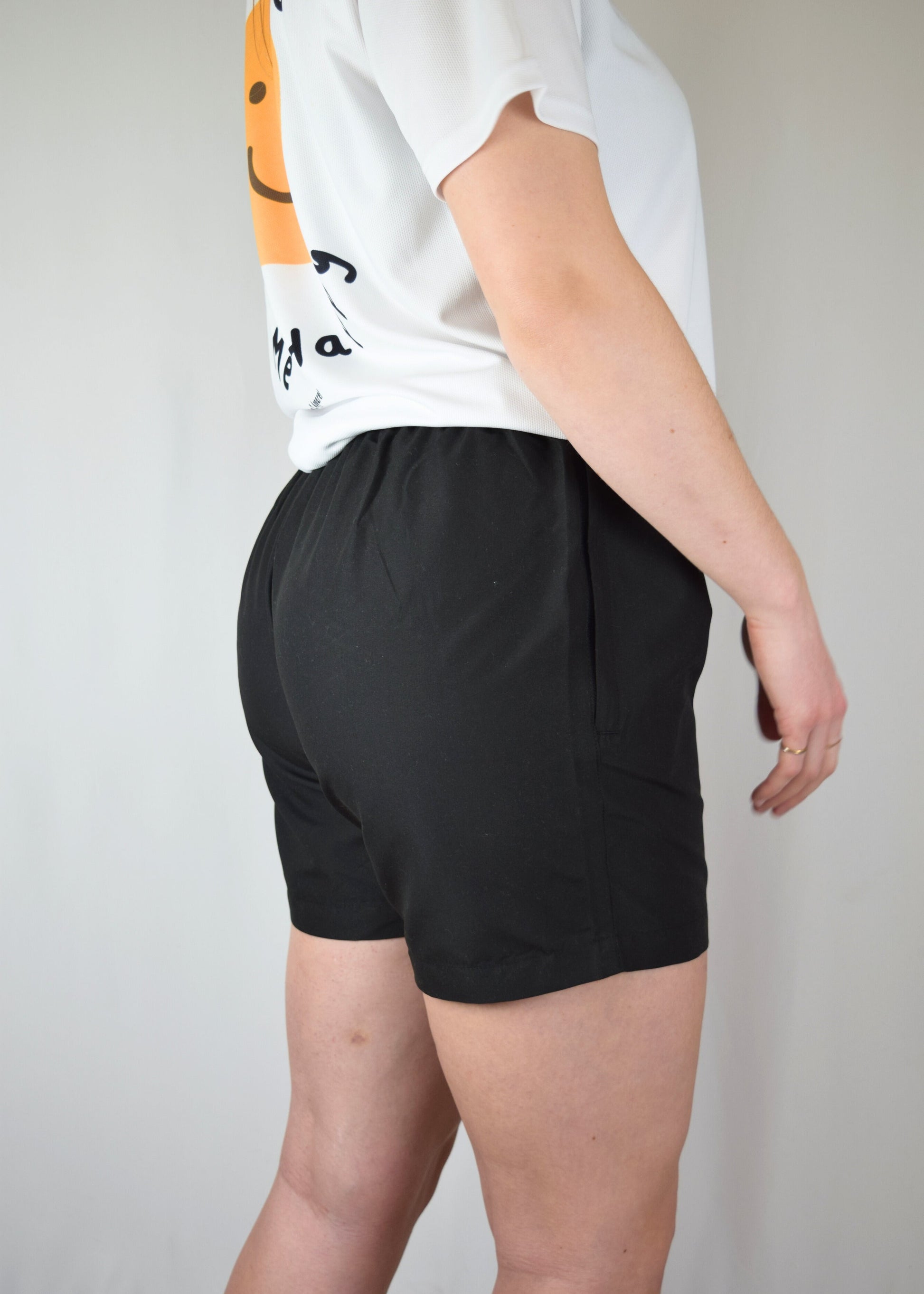 Lady wearing comfortable black athletic shorts with 'Z2' logo and a white shirt with a visible brand logo on a plain background