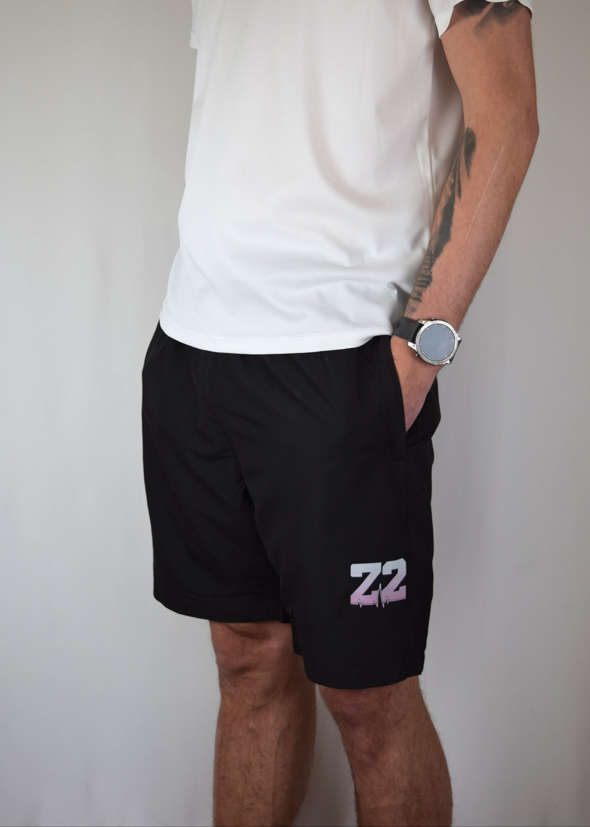 Man wearing comfortable black athletic shorts with 'Z2' logo and a white shirt with a visible brand logo on a plain background
