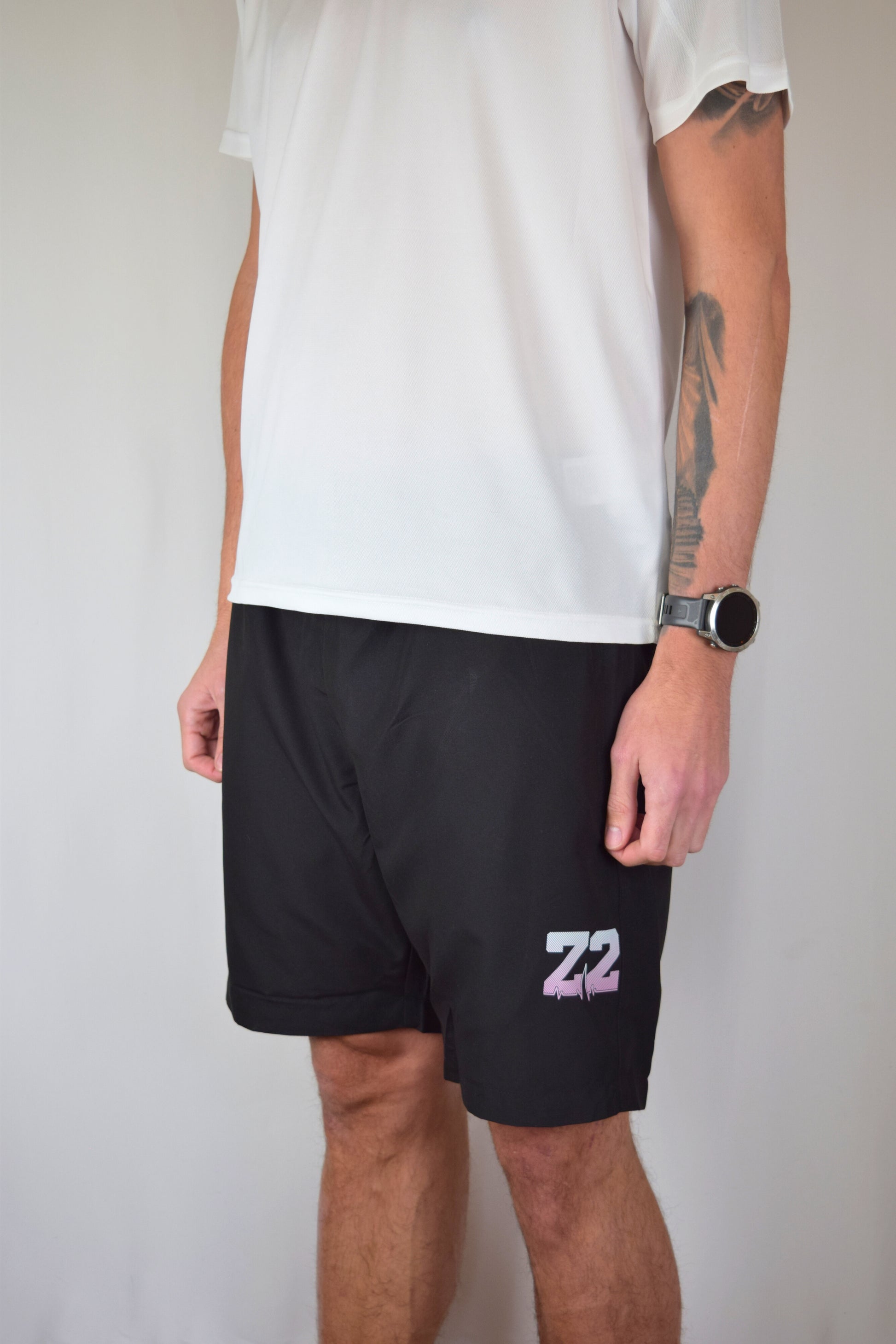 Man wearing comfortable black athletic shorts with 'Z2' logo and a white shirt with a visible brand logo on a plain background