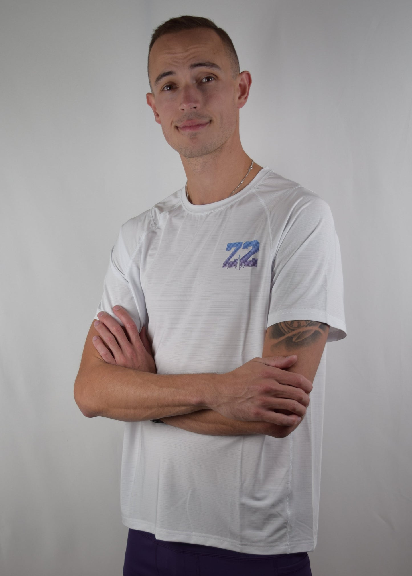 Core performance running top in white, with a purple Z2 logo on the front, and the model has his arms crossed.